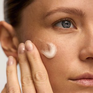 Nahaufnahme einer Frau, die mit ihrer Hand Absolute Silk Micro Mousse Treatment auf ihr Gesicht aufträgt